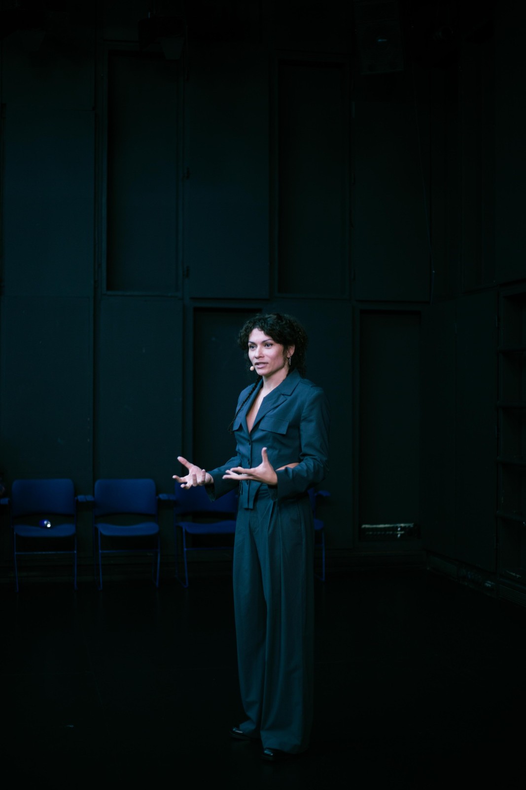 Eine Frau steht in einem eleganten, grünen Zweiteiler auf einer Bühne und erzählt etwas ausdrucksstark.