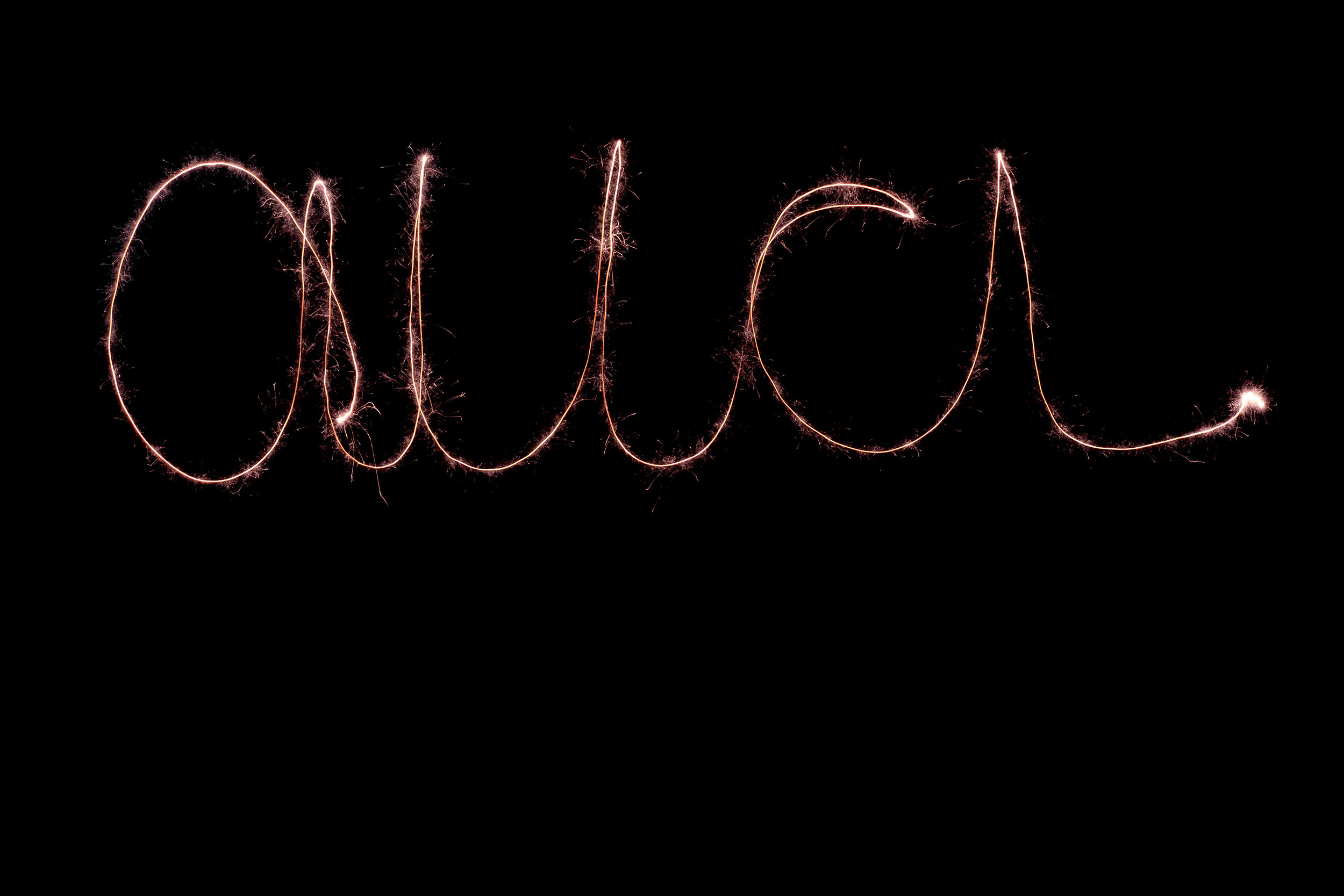 Man sieht das Wort "aua" mit einer Wunderkerze in die Luft geschrieben. Die Schrift leuchtet auf einem schwarzen Hintergrund.
