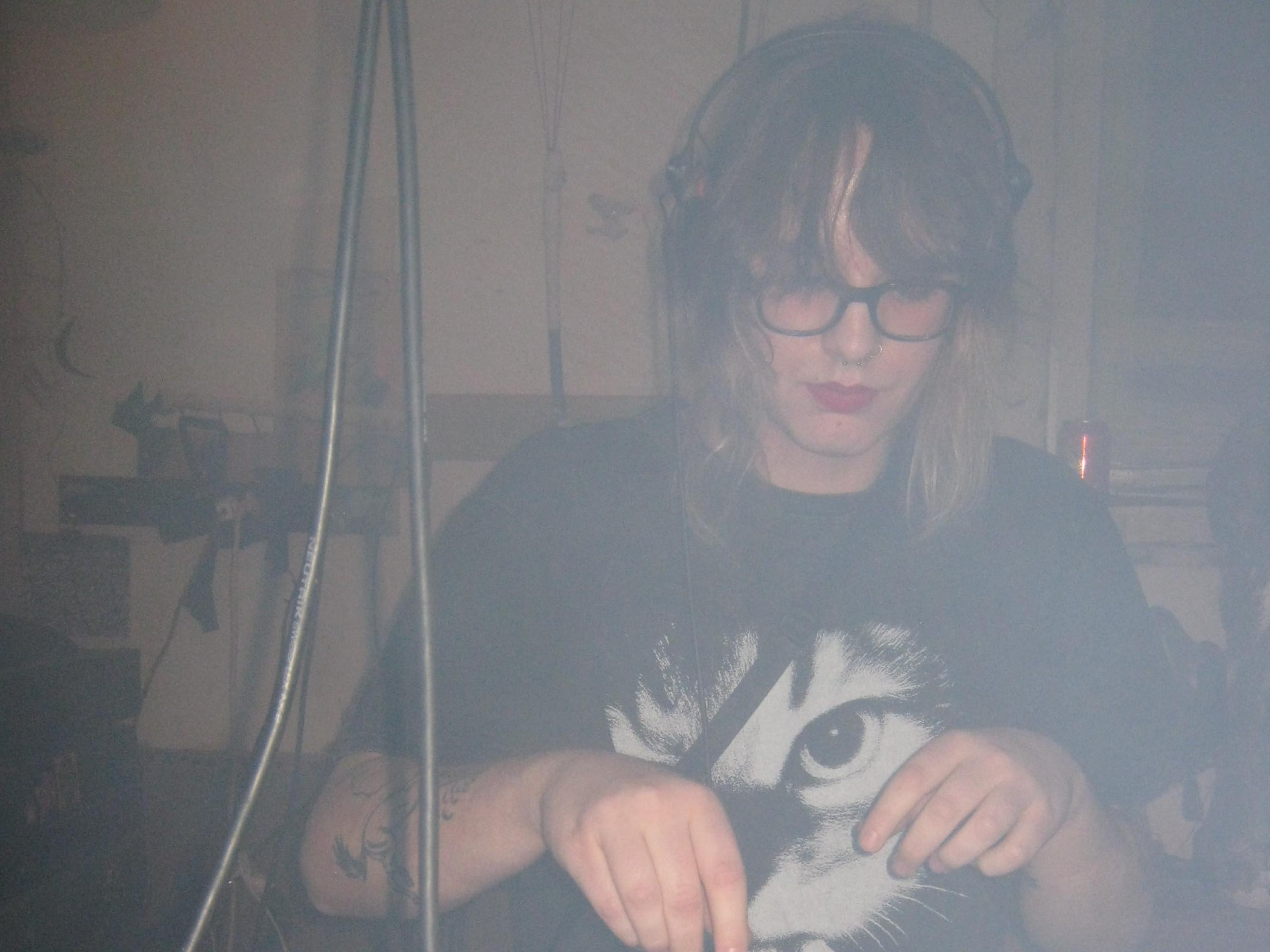 Eine Person mit schulterlangem Haar und Kopfhörern auf spielt an einem Pioneer-Mischer Musik als DJ.