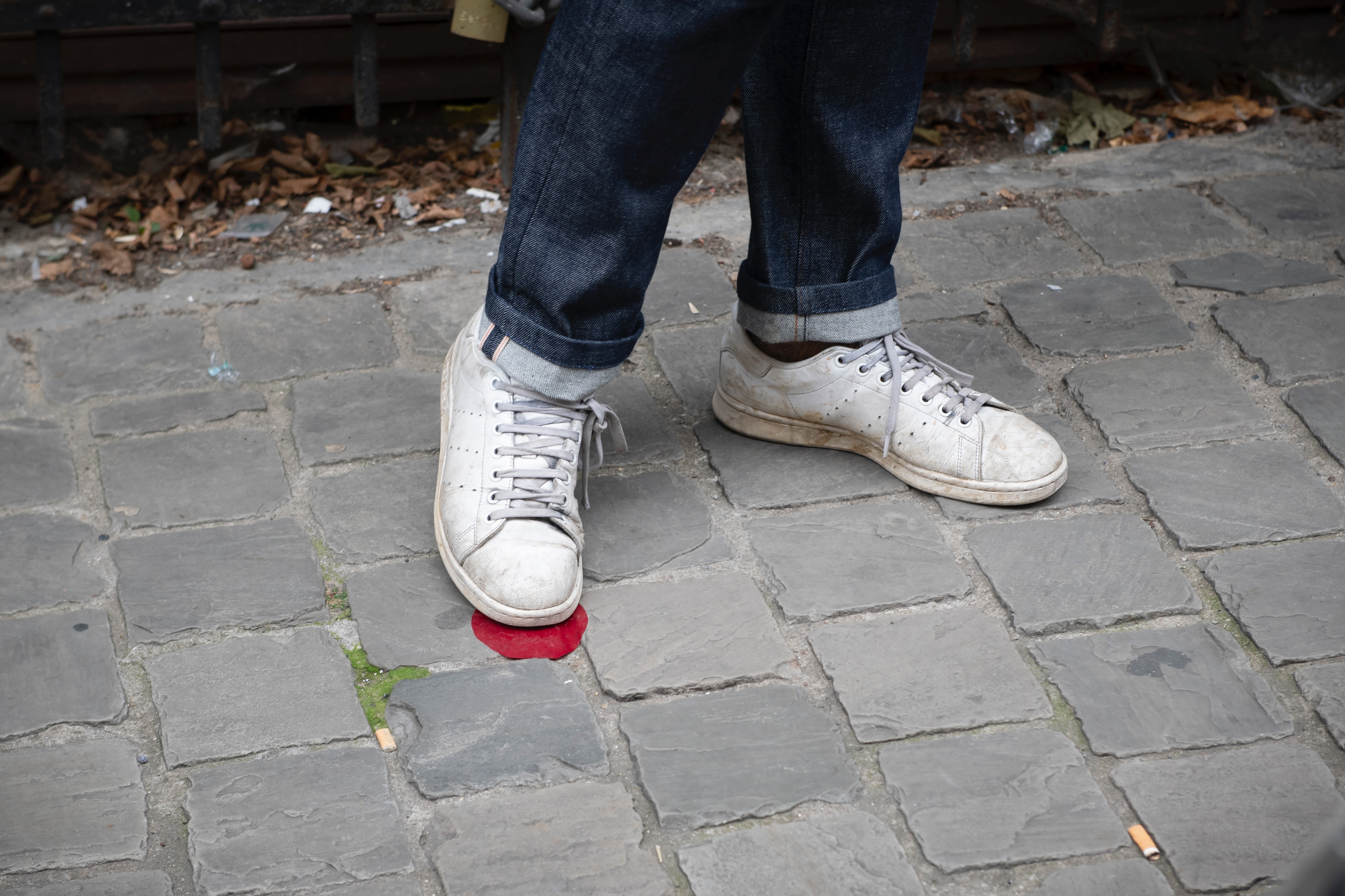 Weisse Schuhe, die auf einem roten Punkt stehen, der auf dem Pflasterstein angebracht ist.